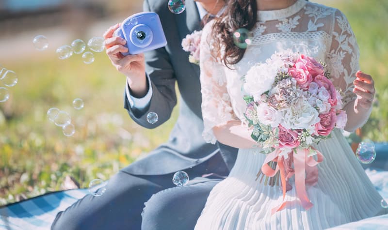 シャボン玉を吹く新郎新婦とピンクのウエディングブーケ画像