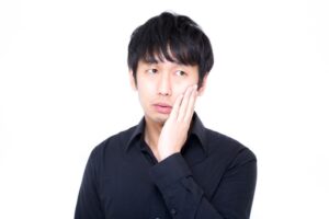 頬に手を当てて悩む黒シャツの男性の画像
