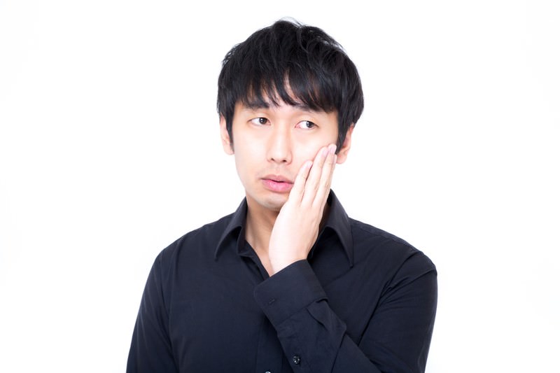 頬に手を当てて悩む黒シャツの男性の画像